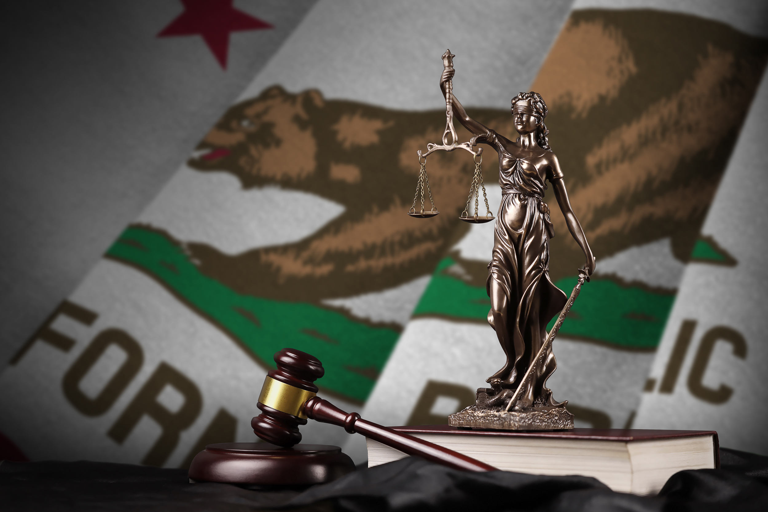 California US state flag with statue of lady justice, constitution and judge hammer on black drapery. Concept of judgement and guilt